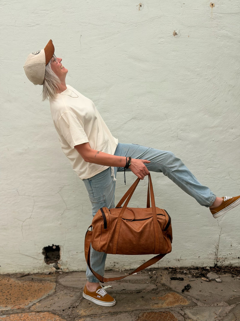 Person holding a brown gemmer leather bag against a white brick wall.